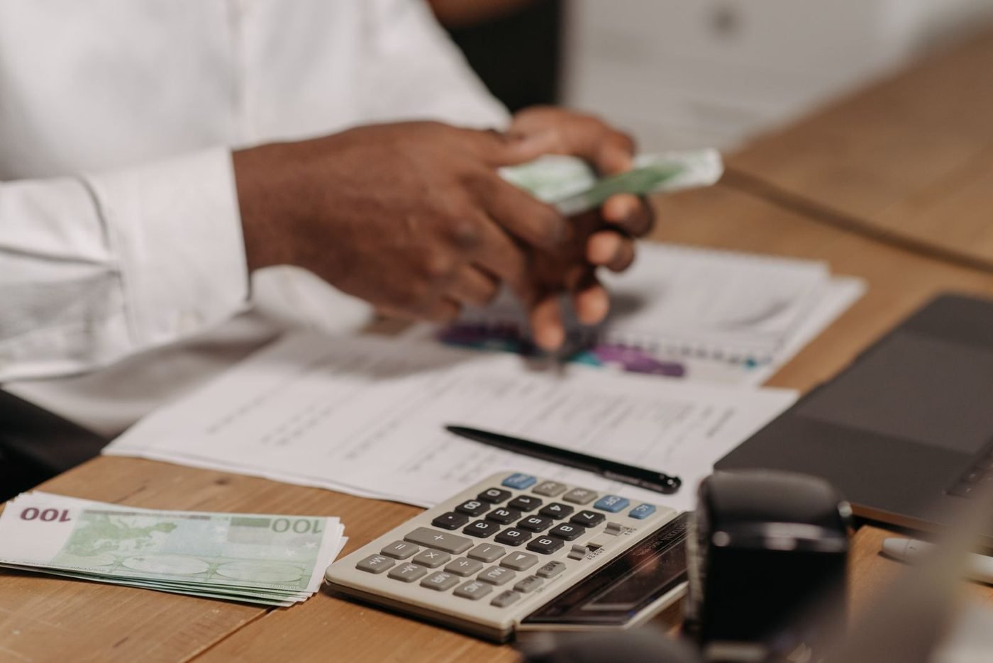 Mains comptant des billets en euros sur un bureau avec une calculatrice et des documents financiers