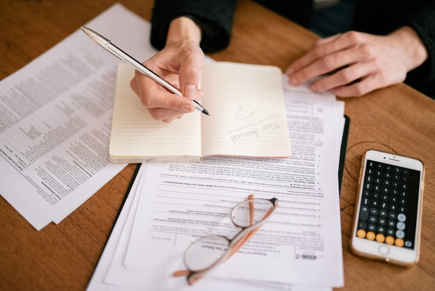 Gros plan d'une personne écrivant dans un carnet avec des documents et une calculatrice, gérant des finances